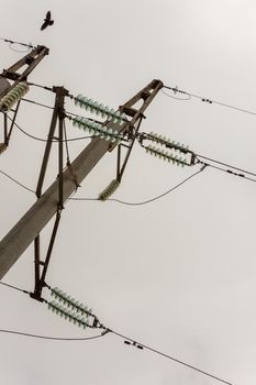 High voltage power line pole with glass electrical insulators on wires at cloudy weather, view from ground surface