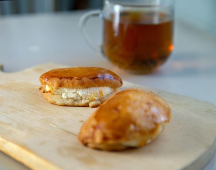 Two pies on wooden tray next to mug of tea on light table. Selective focus