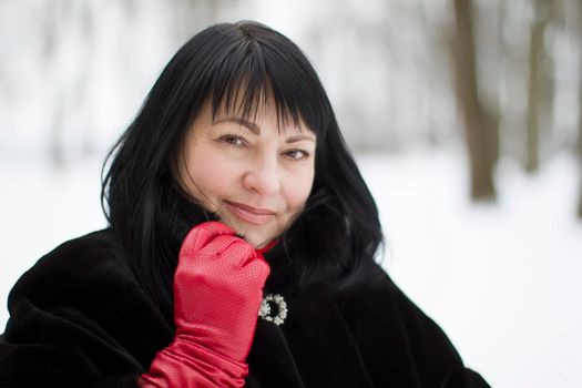 Portrait of a beautiful old woman in a fur coat in red gloves