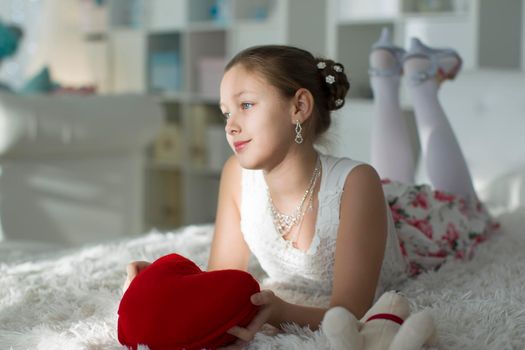 Very beautiful teen girl lying on a bed with a red heart pillow.Young lady