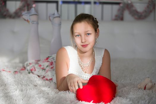 Very beautiful teen girl lying on a bed with a red heart pillow.Young lady
