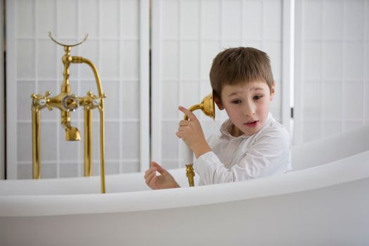 Baby in the bathroom in clothes.The boy sits in the bath and plays the phone.Talking on the phone