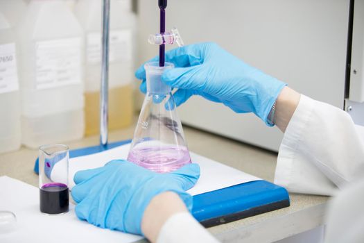 The hands of a technician in blue rubber gloves are holding a flask. Pharmaceutical industry. Chemical laboratory