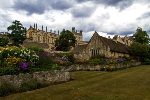 Wide-shot of Christ Church College from a lawn with some houses and flowers in the foreground on a cludy day