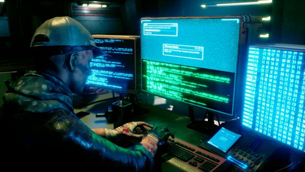 A male hacker surrounded by glowing monitors hacks into someone else's computer network in a dark room of his office. A view of the hacker's futuristic computer office.