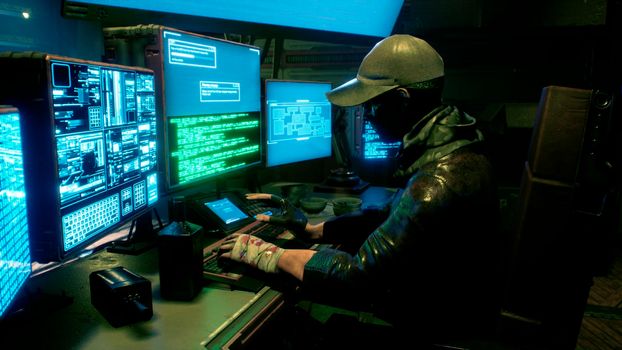 A male hacker surrounded by glowing monitors hacks into someone else's computer network in a dark room of his office. A view of the hacker's futuristic computer office.