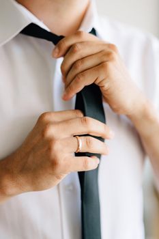 A man puts on and ties a tie while preparing for a wedding ceremony, close-up . High quality photo