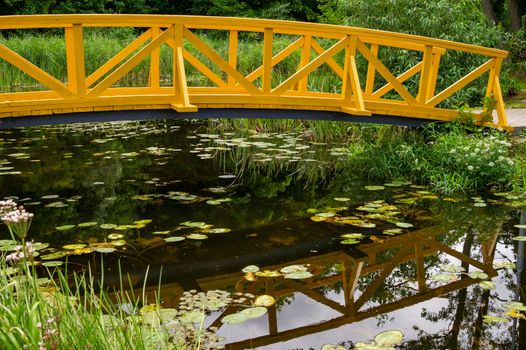 Arched wooden pedestrian bridge curving away and reflections in pond water