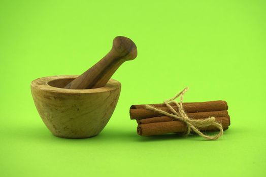 Cinnamon sticks bundle tied with jute string and wooden mortar with pestle on green background and free copy space for text