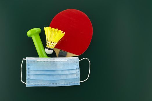 Dumbbells, shuttlecock, table tennis racket cover with a medical face mask. Sports during the quarantine period concept with free copy space