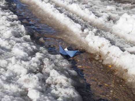 Paper boat sails through meltwater on spring day.