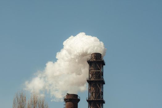 Two industrial pipes with thick smoke coming out of them. Environmental pollution. Against the blue sky.