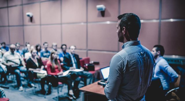 Speaker giving a talk on corporate business conference. Unrecognizable people in audience at conference hall. Business and Entrepreneurship event.