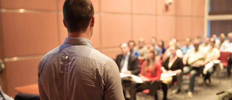 Speaker giving a talk on corporate business conference. Unrecognizable people in audience at conference hall. Business and Entrepreneurship event.