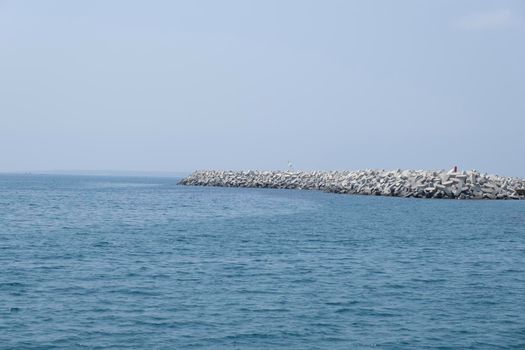 Aerial shot of the open sea on a cloudy day. Blue sky, pier, ships in the distance and boundless horizon.