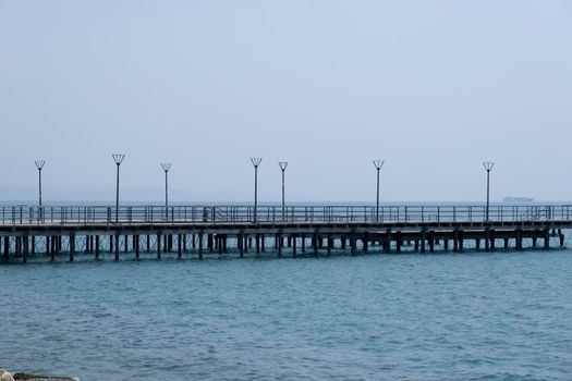 Shot of the open sea on a clear sunny day. Blue sky, pier, ships in the distance and boundless horizon.