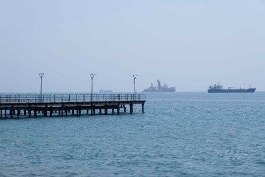 Shot of the open sea on a clear sunny day. Blue sky, pier, ships in the distance and boundless horizon.