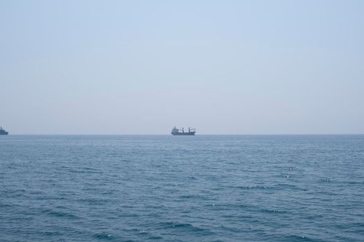 Aerial shot of the open sea on a cloudy day. Blue sky, pier, ships in the distance and boundless horizon.