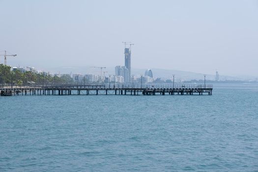 Aerial shot of the open sea on a cloudy day. Blue sky, pier, ships in the distance and boundless horizon.