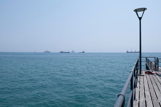 Shot of the open sea on a clear sunny day. Blue sky, pier, ships in the distance and boundless horizon.