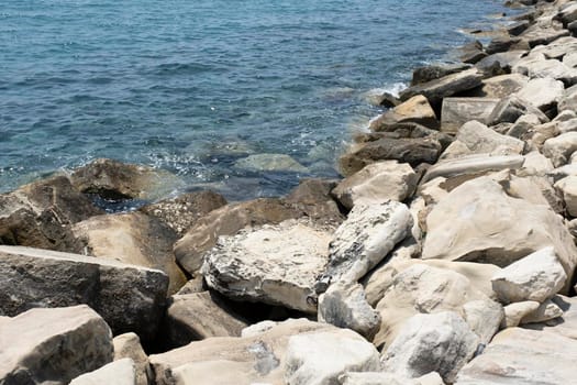 Close-up of a stone beach on a clear day. Rocks and pebbles on the beach, flooded with sea spray and waves.