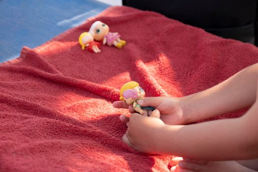 Cute girl playing with her dolls on a sunbed on a sandy beach on a sunny day.