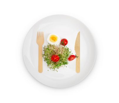 Heap of alfalfa sprouts on a white plate with a wooden fork and knife. Healthy food concept. Isolated on white background with clipping path.