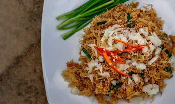 Asian eating food, Mee Grob is an sweet and sour crispy noodles, made from Thai rice noodle with sweet and sour sauce on white plate, Sweet & Sour Crispy Rice Noodles, Close up.