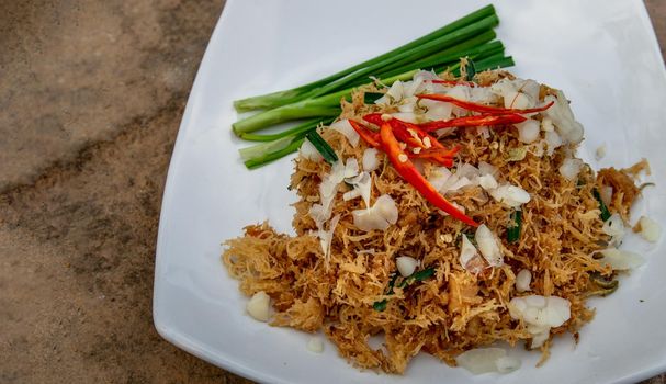 Asian eating food, Mee Grob is an sweet and sour crispy noodles, made from Thai rice noodle with sweet and sour sauce on white plate, Sweet & Sour Crispy Rice Noodles, Oblique view from the top.