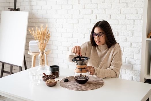Alternative coffee brewing. Young woman brewing coffee in chemex standing at the white table with various stuff for alternative coffee brewing, pouring hot water into the filter
