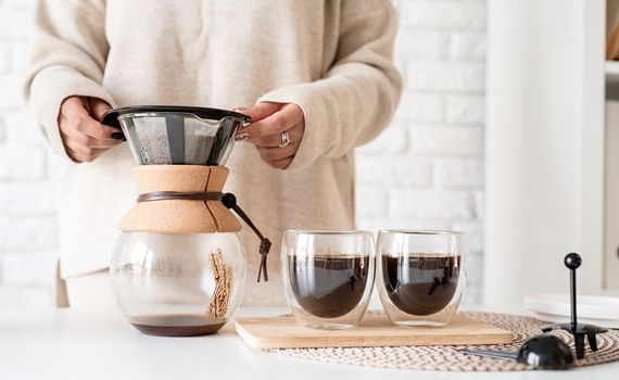 Alternative coffee brewing. Young brunette woman drinking hot black coffee sitting at the white table