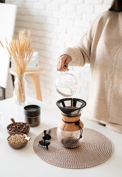 Alternative coffee brewing. Young woman brewing coffee in chemex standing at the white table with various stuff for alternative coffee brewing, pouring hot water into the filter