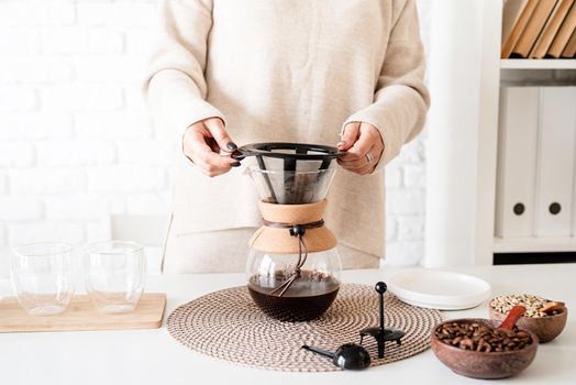 Alternative coffee brewing. Young woman brewing coffee in chemex standing at the white table with various stuff for alternative coffee brewing