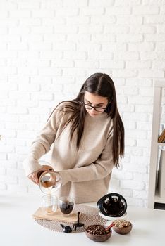 Alternative coffee brewing. Young woman brewing coffee in chemex standing at the white table with various stuff for alternative coffee brewing, pouring coffee to the glass