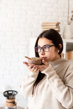 Alternative coffee brewing. Young brunette woman brewing coffee in chemex, smelling green coffee beans