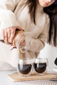 Alternative coffee brewing. Young woman brewing coffee in chemex standing at the white table with various stuff for alternative coffee brewing, pouring coffee to the glass