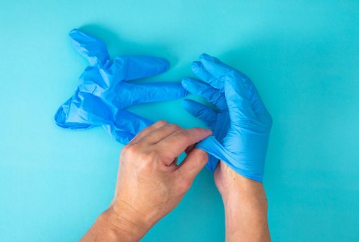 hands remove glove on blue background. The concept of treatment, protection from viruses, flu, recovery, stop coronavirus.