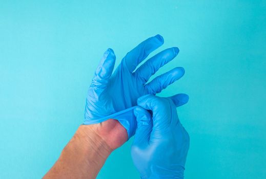 hands remove glove on blue background. The concept of treatment, protection from viruses, flu, recovery, stop coronavirus.