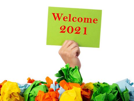 Hand holding a green paper with word Welcome 2021 comimg out from the crumble paper.