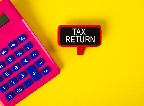 Top view of calculator and a tag with TAX RETURN word on yellow background
