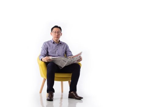 An Asian man seated in an armchair reading a newspaper isolated on white background