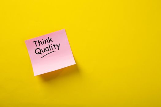 Think Quality word concept on sticky note against yellow background