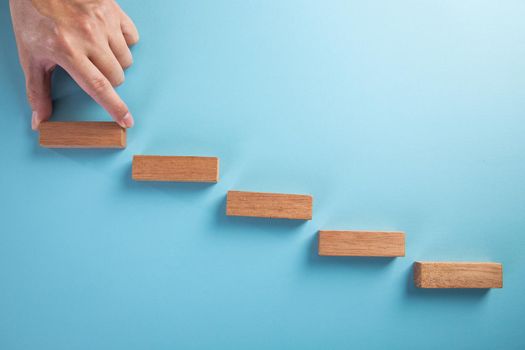 Concept of business development stages. Hand holds wooden block on blue background