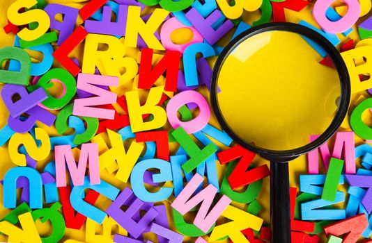 Magnifying glass with colorful alphabet on yellow background.Education concept.