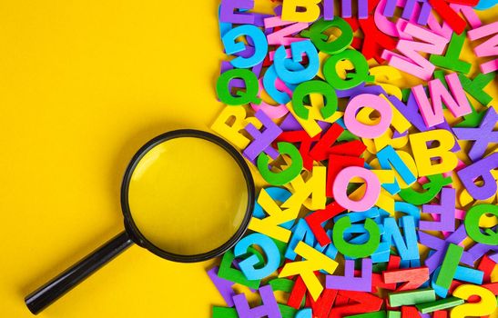 Magnifying glass with colorful alphabet on yellow background.Education concept.