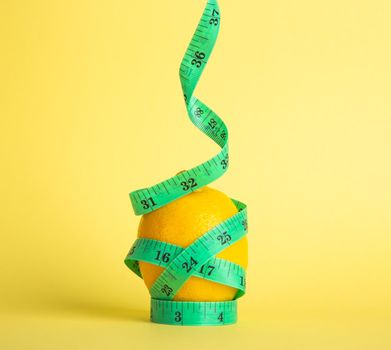 Diet concept. Lemon and tape measure on yellow background