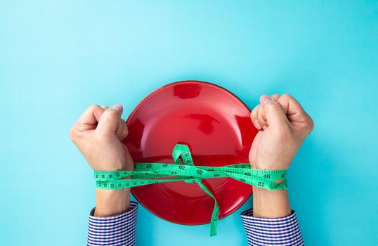 Tied hands of a man with a measuring tape and empty plate. Willpower for losing weight.