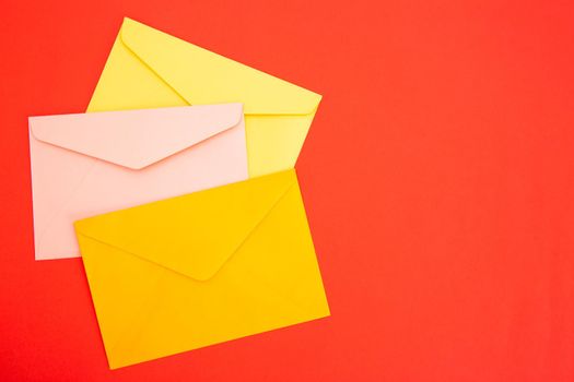 Colorful paper envelopes on red background - top view