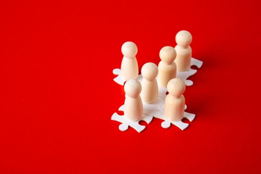 Wooden figures on puzzles on red background as a symbol of team building. Organization group people in business. Cooperation and partnership.