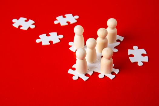 Wooden figures on puzzles on red background as a symbol of team building. Organization group people in business. Cooperation and partnership.